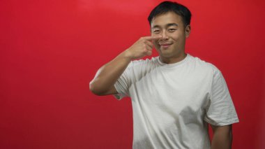 Çinli bir adam kırmızı bir stüdyo duvarına karşı burun buruna gülümserken mutluluğu işaret ediyor..