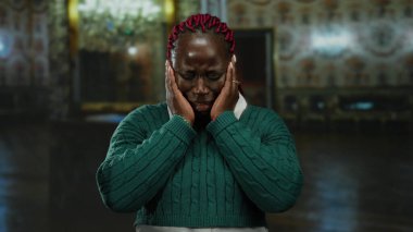 Yeşil kazaklı bir kadın müzede avize ve dekorasyonla iç mekanda ağlıyor. Kültür ortamında duygu ve iç gözlem uyandırıyor..