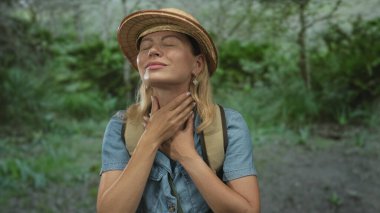 Kadın boynuna dokunuyor ve sırt çantasını hasır şapkanın altında tutuyor. Ormanda güneşli yeşil eğrelti otları arasında. Huzur, sükunet, huzur ve huzur..