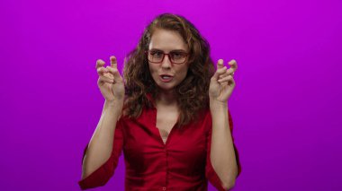 Kırmızı tişörtlü, gözlüklü bir kadın, parlak pembe arka planda parmakları olan tırnak işaretleri kullanıyor. İğneleme ve odaklanmış ifade ile alay ediyor..