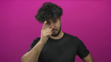 Sakallı genç İspanyol bir adam canlı pembe bir arka plana karşı düşünceli ve odaklanmış görünüyor..