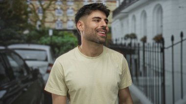 Park halindeki arabaların ve demir çitlerin yanında beyaz tişört giyen gülümseyen bir adam yüzü..