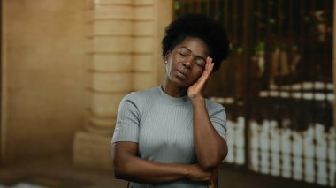 Şehir caddesinde kolları çapraz duran gri süveter giymiş bir kadın.