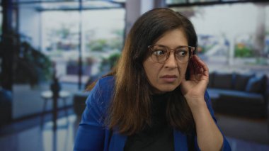 Gözlüklü ve mavi ceketli İspanyol kadın otel lobisinde konuşurken el hareketi yapıyor..