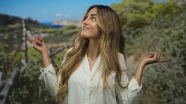 Genç sarışın kadın iki parmağını da güneş ışığıyla aydınlanan üzüm bağı yamacını işaret ediyor..