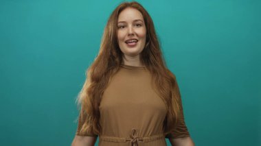 Stüdyoda uzun kızıl saçlı kadın gülümsüyor ve ellerini başının üstünde bir kalbe dönüştürüyor..