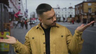 Genç ispanyol adam kaşlarını çatar ve meşgul şehir caddesinde tuğla binalar tarafından el kaldırır; belirsizlik.