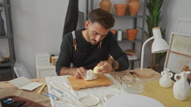 Stüdyoda beyaz çamuru çıplak elle şekillendiren İspanyol genç adam. Konsantrasyon yaratıcılığı..