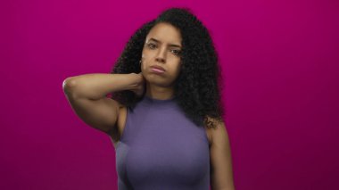 Boyun ağrısından muzdarip bir kadın canlı pembe bir arka planın önünde duruyor ve bir rahatsızlık ve gerilim anı yakalıyor..