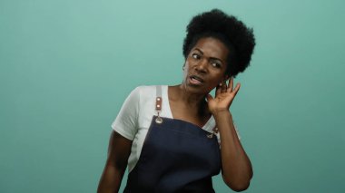 Önlüklü kadın yeşil arka planda dikkatle dinliyor, merak ve nişan gösteriyor..