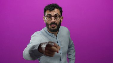 Sakallı ve gözlüklü İspanyol bir adam canlı pembe bir arka plana karşı güçlü duygular taşıyor..