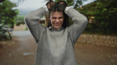 Gri kazaklı kadın, güneşli bir günde arka planda bulanık ağaçlar ve patika olan parkta hayal kırıklığını ifade ediyor..