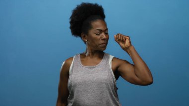 İzole edilmiş mavi arka planda kaslarını kasan kadın güç ve güç gösterisi yapıyor..