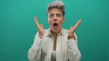 Beyaz gömlekli kadın, turkuaz stüdyoda ağzı açık el kaldırıyor. Sürpriz..