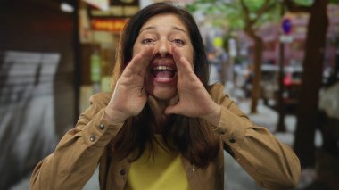 Orta yaşlı İspanyol bir kadın sokakta elleri sımsıkı bağlı bağırıyor; coşkulu bir ses ifadesi var..