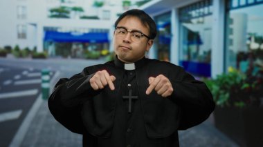 Arka planda binalar olan şehir sokağında duran Asyalı bir adam, aşağı doğru çapraz durarak düşünceli bir jest öneriyor..