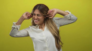 Kadın kulaklarını sarı arka planlı fotoğraf stüdyosunda parmaklarıyla kapatıyor..
