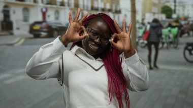 Şehirdeki kadın gülümserken, gözlük takarken ve beyaz örgü örerken normal bir jest yapıyor..