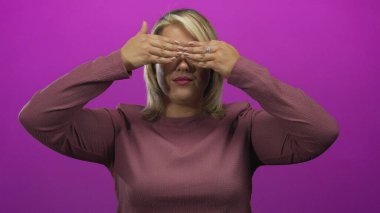 Genç sarışın kadın elleri ile gözlerini kapar ve mor bir stüdyoda gülümsemek için ellerini indirir..