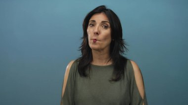 Orta yaşlı, zeytin yeşili bluzlu, siyah saçlı, dudak çantalı ve başını stüdyoya doğru eğmiş bir İspanyol kadın..