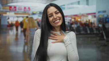 Havaalanında gülümseyen bir kadın, hareketli bir arka planı olan, yoğun terminal ve oturma alanlarında seyahat etmeye hazır ve mutlu bir şekilde..