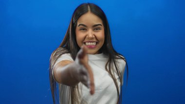 Gülümseyen ve el sıkışan bir kadın canlı mavi arka planda izole edilmiş. Stüdyo ortamında dostane bir hoş geldin davranışı izlenimi veriyor.