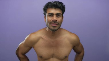 Latin asıllı genç adam mor stüdyoda çıplak göğüs ve ellerle öne eğiliyor; fiziksel rahatsızlık..