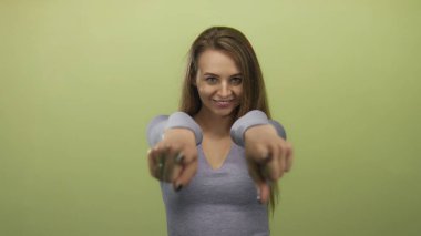 Neşeli sarı arka planda poz veren kadın, iki eliyle kameraya doğru hareket ederken neşeli ve kendinden emin bir ifade yansıtıyor..