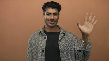 Kareli gömlekli, gülümseyen İspanyol adam turuncu duvara karşı stüdyoda el ele dalgalanıyor..