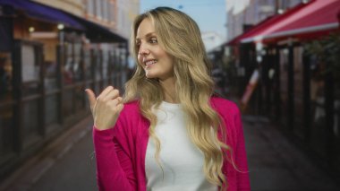 Restoran terasında gülümseyen pembe süveter giyen bir kadın şehir sokağında sarı saçlı, güpegündüz gideceği yeri gösteren bir el gösteren bir kadın..