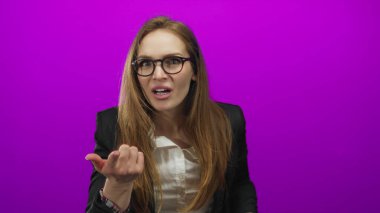 Mor bir stüdyoda gözlük takan ve elleri ağzı kapalı bir ceket giyen genç bir kadın. Sürpriz..