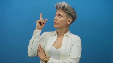Beyaz gömlek giyen, stüdyoda parmaklarını sağa sola gösteren kadın, merak uyandıran içgörü yansıması.