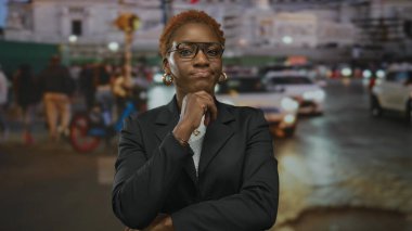 Elleri çenesinde olan kadın, bulanık arabalar ve sokak lambaları arasında kalabalık şehir merkezi caddesinde gece ayakta duruyor..