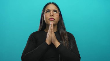 Kadın sakin bir şekilde meditasyon yapıyor gözleri kapalı ve elleri mudra pozisyonunda izole edilmiş yeşil bir arka plan üzerinde, sakin bir ortamda gözlük ve siyah kıyafetler giyiyor..