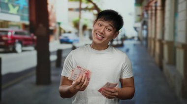 Kalabalık bir şehir caddesinde Tayvan doları tutan genç adam, gün boyunca şehir dışında dururken gülümsüyor..