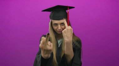 Mezuniyet şapkalı ve cüppeli kadın pembe arka planda cesur bir hareket yapıyor..