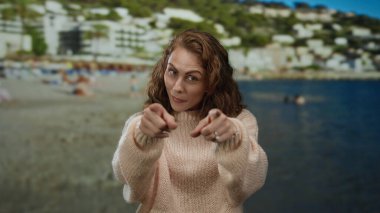 Hareketli bir sahil sahilinde gülümseyen bir kadın açık mavi bir gökyüzünün altında insanlarla dolu rahat bir süveter ve tepeler giyiyor..