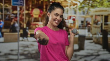 Pembe tişörtlü bir panayır atlıkarıncasında el sıkışan ve 1 kilo ağırlığında dambıl tutan bir kadın, dostluğu selamlıyor..