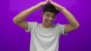 Gülümseyen adam mor stüdyoda çatı jesti oluşturmak için kollarını kaldırır; sevinç kutlaması yaratıcılığı.