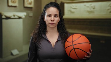 Kapalı müze ortamında basketbol tutan bir kadın, sanatsal sergilerin arasında genç İspanyol gençliğini sergileyen bir kadın..