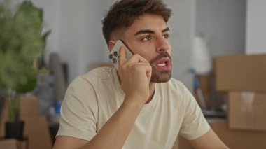 Adam binanın içindeki kutuları açarken masaya yaslanırken akıllı telefonu kulağına tutuyor; tefekkür.