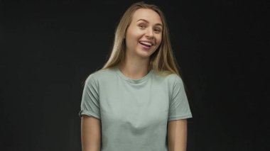 Uzun saçlı beyaz bir kadın izole edilmiş siyah arka plan duvarına karşı gülümsüyor. Günlük gömlek giyiyor. Stüdyo ortamında mutlu ve mutlu görünüyor.