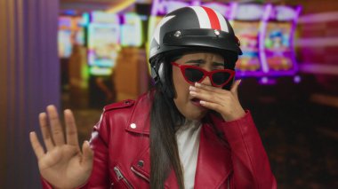 Kumarhanede, bir kumar makinesinin yanında kask takan bir kadın yüzünü tiksintiyle kapatıyor. Genç Latin sürprizi hissediyor..