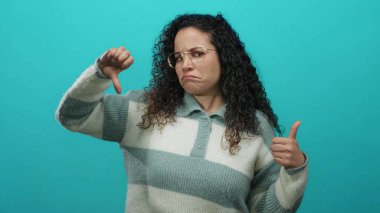 İzole edilmiş yeşil arka plan duvarının önünde, gözlüklü ve çizgili kazaklı karışık duyguları ifade eden genç bir kadın..