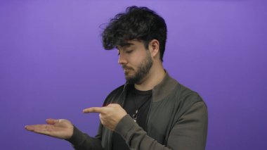 Avuç içinin açık olduğunu gösteren sakallı, koyu renk ceketli, siyah ceketli, meraklı ya da sunum yapan genç bir İspanyol..