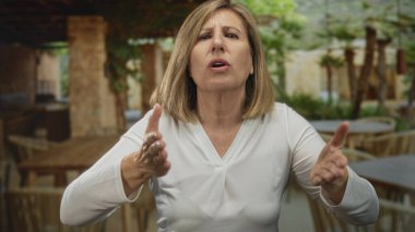 Teras inşaatında kameraya bakan bir kadın, iki elini de açık ağızla kaldırıyor..