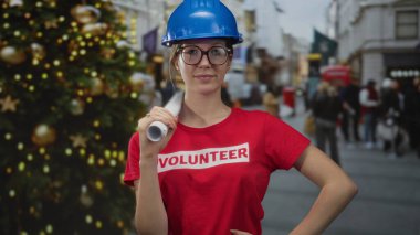 Kadın yuvarlanmış planı tutuyor ve mühendis kaskı takarak gözlük ayarlıyor; servis ruhu umudu.