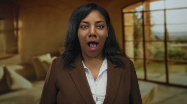 Oturma odasında konuşan Afro-Amerikalı kadın kameraya bakıyor..