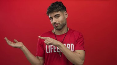 Kırmızı cankurtaran tişörtü giyen İspanyol genç cankurtaran kırmızı stüdyoda çıplak elle işaret ediyor..