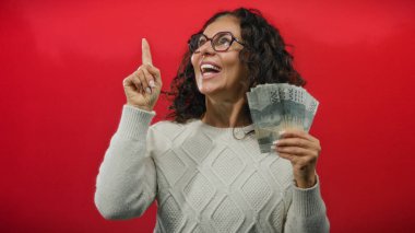 Endonezya rupia banknotları tutan ve canlı kırmızı bir arkaplana doğru bakan, mutluluk ve parasal başarı gösteren bir kadın..